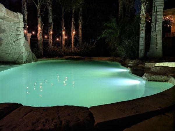 Lagoon-style pool lit up at night by underwater lights