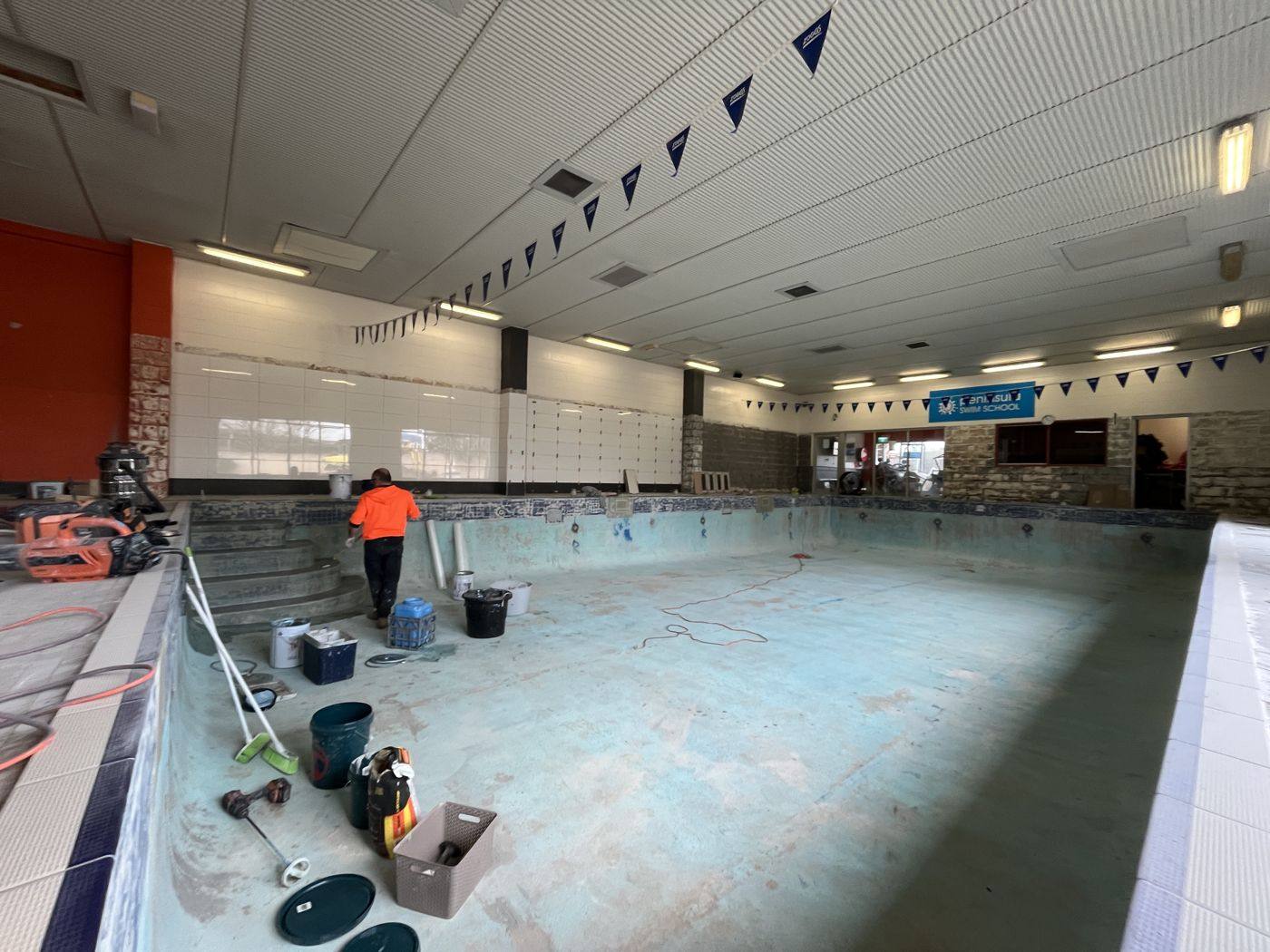 Indoor commercial pool being prepared for resurfacing, with crew and equipment