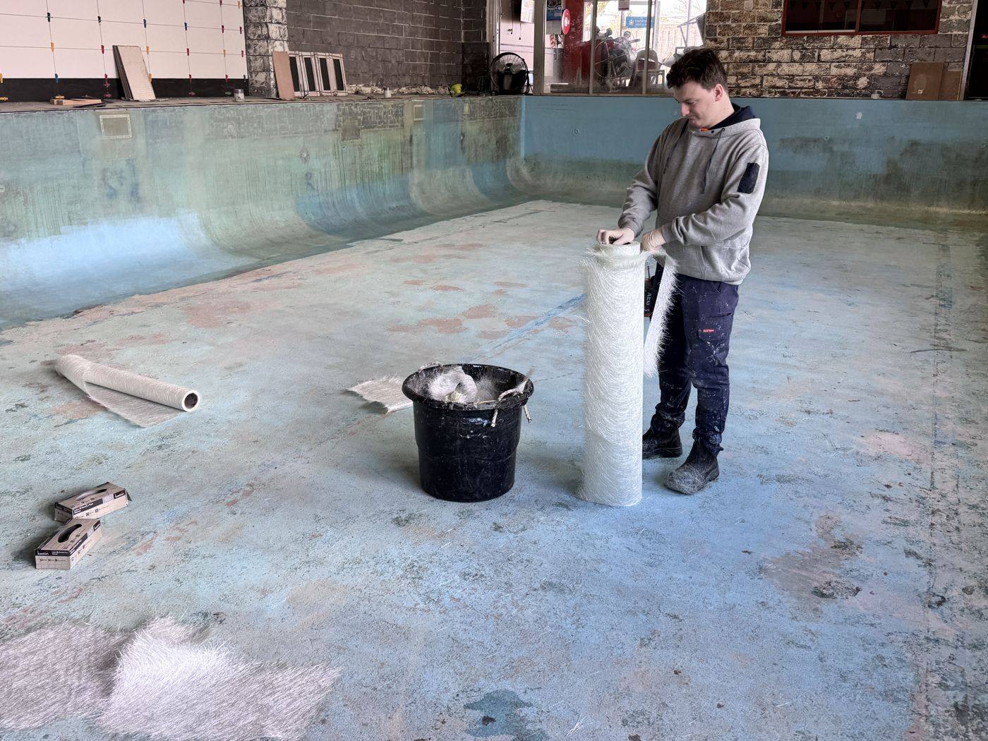 A team member unrolling fibreglass matting in an empty pool