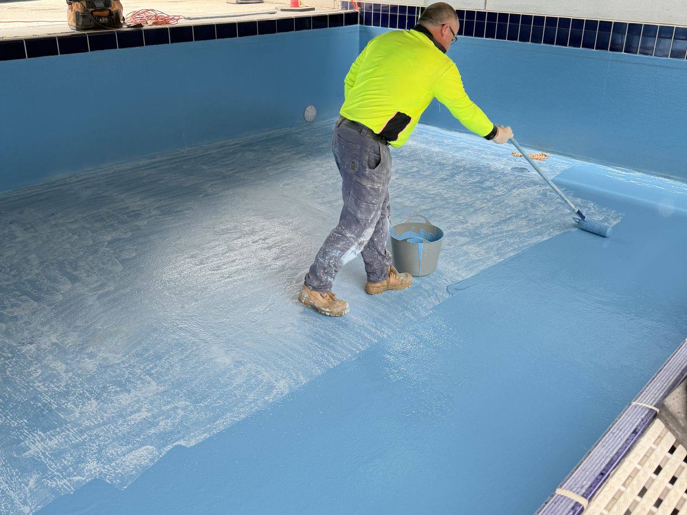 An Australian Pool Resurfacing team member rolling resin over fibreglass matting in an empty pool